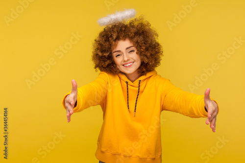 Portrait of kind-hearted generous curly-haired hipster woman with saint nimbus raising hands to embrace, giving free hugs and smiling with love Tableau sur Toile