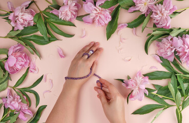 two hands of a young girl with smooth skin and a bouquet of pink peonies on a peach background