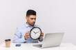 © khosrork - Time management. Displeased man showing clock to laptop screen, having online video call communication, looking strict angry, warning of schedule deadline. studio shot isolated on white background