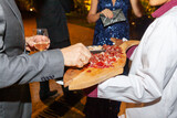 Fototapeta  - La mano de una persona coge una loncha de jamón que le ofrece un camarero en una bandeja de madera