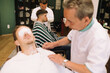 © sealovers - barber cutting the beard of an attractive young brown man with cotton wool in his eyes