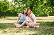 © strekozza77 - Two beautiful girls have fun in the park on a sunny summer day. The sisters are sitting on a green lawn, laughing.