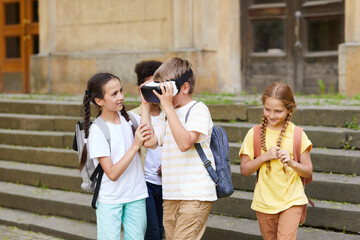 Wall Mural - Multi-ethnic group of cheerful school children playing with VR glasses outdoors, focus on boy wearing gear, copy space