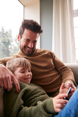 Father And Son On Sofa At Home Having Fun Playing Game On Mobile Phone