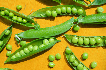 Ripe peas in pods on a yellow wooden background. The concept of summer, pea crop, healthy vitamin food.