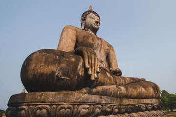 The large old Buddha statue Enshrined stands majestically in the Sukhothai Historical Park. Amid the orange-coloured sky during the evening, Sukhothai Province, Thailand