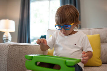 little boy playing iPad wearing blue light blocking glasses