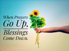 Inspirational Quote - When Prayers Go Up, Blessings Come Down.  With Hand Holding Bouquet Of Sunflowers Against Bright Blue Sky Background. Prayer And Blessing Text Message Concept.
