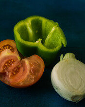 
A Red Tomato, A Green Pepper And A White Onion, Cut, On A Blue Background. Vertical Format.