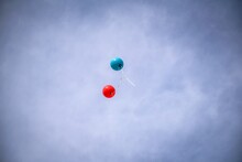 Low Angle Shot Of A Blue And Red Balloons Floating Away On A Blue Sky Background