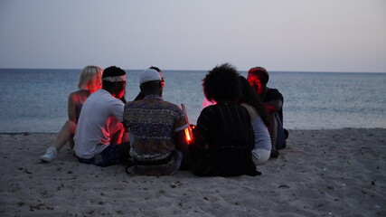 leisure and people concept - group of smiling friends sitting at camp fire on beach at night