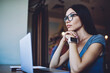 © BullRun - Pensive female student in stylish spectacles feeling pondering about e learning and software updating on modern netbook, thoughtful woman thinking while sitting with computer in coworking space