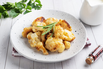 Fried cauliflower florets in batter on a white plate. White wooden background.