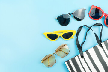 Wall Mural - color fashion sunglasses and paper bag arranged on blue background with copy space,shopping concept