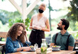 © Halfpoint - Waitress with face mask serving happy couple outdoors on terrace restaurant.