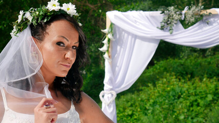 Porter of a bride with a flower wreath on her head and veil in front of the wedding ceremony arc.