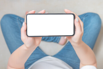 Poster - Mockup image blank white screen cell phone. female hands holding texting using mobile phone on sofa at home. cell phone in horizontal position. Empty space for advertise text.