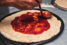 Chef Applying Tomato Sauce With A Ladle On Pizza Dough