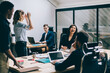 © BullRun - Multicultural male and female office employees dressed in formal wear having fun sitting at working place in finance company.Positive modern colleagues laughing while talking about funny project