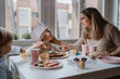 © Angel Santamaria/ADDICTIVE STOCK - Positive mother in casual clothes sitting at wooden table and talking with kids celebrating birthday at home