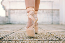 Crop Female Dancer Wearing Pointe Shoes Standing On Tiptoes On Weathered Stone Ground And Demonstrating Dancing Position