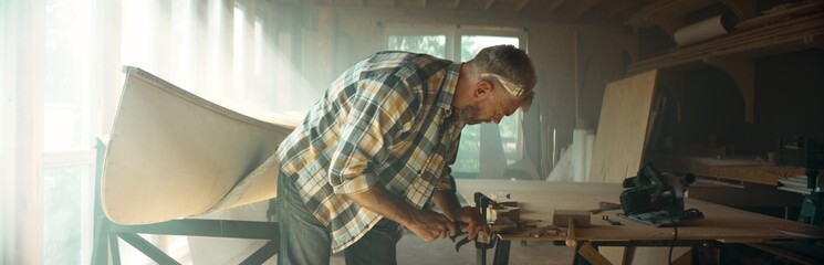 Wall Mural - Caucasian male shaping canoe paddle with a chisel in his workshop. Boat making hobby