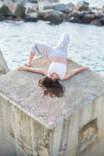 From Above Of Relaxed Young Female In White Sportswear Lying On Concrete Block Of Coastal Breakwater In Sunlight