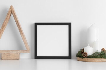 Sticker - Black square frame mockup with a wooden tree and candles on a white table. Christmas decoration.