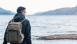 © Pol Sole/ADDICTIVE STOCK - Back view of male hiker in warm jacket with backpack sitting on wooden bench near sea and enjoying marine scenery with rocky coast during travel in Scotland