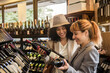 © Widetape/ADDICTIVE STOCK - Side view of cheerful diverse woman exploring shelves of wine market with bottles choosing wine.