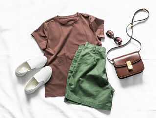 Women's cotton bermuda shorts, brown t-shirt, crossbody bag, white leather sneakers on a light background, top view. Fashion concept