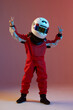 © Georgii - Cool boy child racer in helmet with raised hands with peace gesture, standing in neon light. Kart racing school poster
