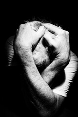 Man depressed, grieving, crying, mental break down, alone in a dark place covering head and face with hands and arms surrounded by darkness, B&W, black & white high contrast and hard shadows