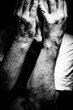 Man suffering depression, anguish or mental health alone covering face with hands and arms surrounded by darkness done in black & white monochrome high contrast and hard shadows soft focus