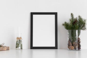 Sticker - Black frame mockup with a bouquet of fir, candle and a gift on a white table. Christmas decoration.