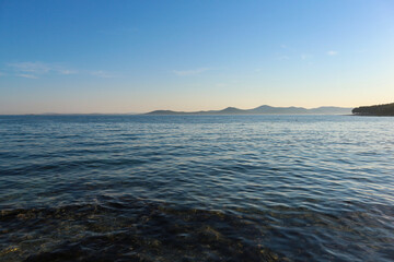 Canvas Print - Peaceful, crystal clear, blue adriatic sea at sunset off the Pakostane town shore, with rows of islands in the distance on the horizon