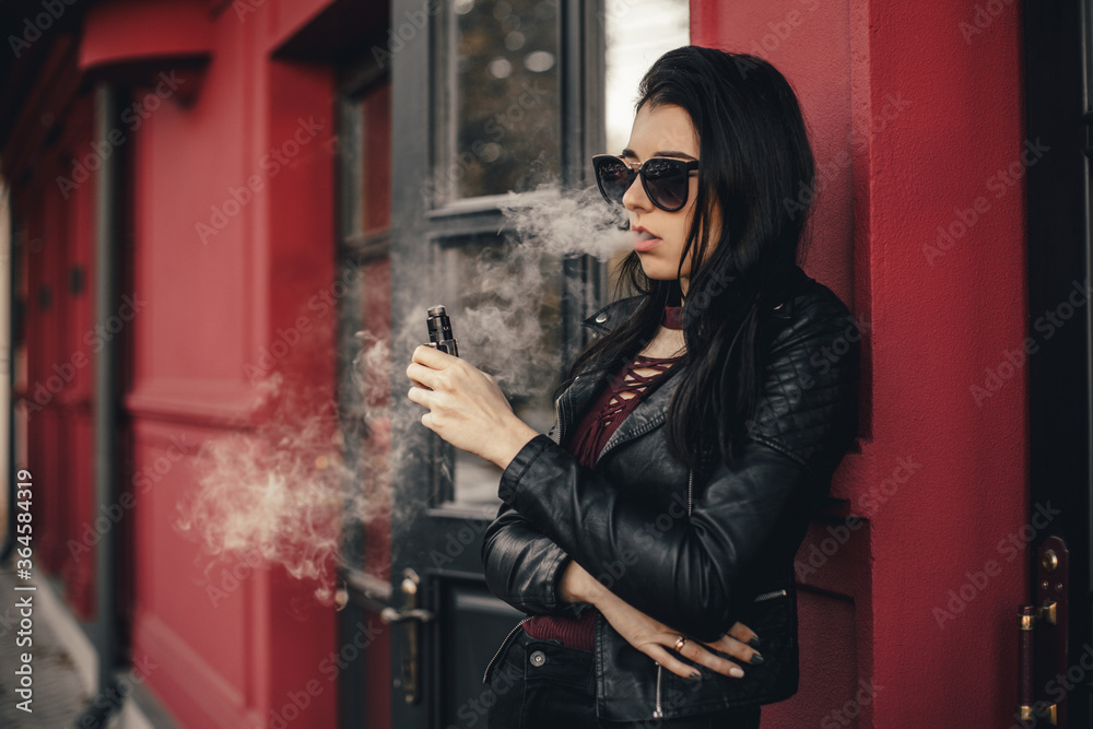 elfbar nachfüll pod läuft aus Beautiful stylish brunette smoking an e-cigarette as she is walkind through  the city. Vaping concept. Trendy new vaping device, smoke e-liquid instead  of nicotine cigarettes. Stock Photo