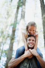 Wall Mural - Smiling father carrying daughter on shoulders in woods