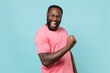 © ViDi Studio - Happy young african american man guy in casual pink t-shirt posing isolated on pastel blue background studio portrait. People emotions lifestyle concept. Mock up copy space. Doing winner gesture.
