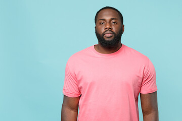 Wall Mural - Young african american man guy in casual pink t-shirt posing isolated on pastel blue wall background studio portrait. People sincere emotions lifestyle concept. Mock up copy space. Looking camera.