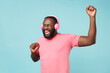 © ViDi Studio - Funny young african american man guy in casual pink t-shirt isolated on blue background studio. People lifestyle concept. Mock up copy space. Listen music with headphones keeping eyes closed, dancing.