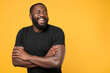 © ViDi Studio - Laughing african american man guy football fan in casual black t-shirt isolated on yellow background studio portrait. People lifestyle concept. Mock up copy space. Holding hands crossed looking aside.