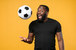 © ViDi Studio - Excited african american man guy football fan in casual black t-shirt isolated on yellow background. Sport family leisure lifestyle concept. Cheer up support favorite team throwing up soccer ball.