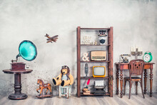 Antiques Still Life With Old Gramophone, Teddy Bear, Rocking Horse And Collection Of Outdated Media, News Makers And Writers Devices Front Concrete Wall Background. Vintage Style Filtered Photo