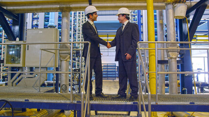 two businessmen shaking hands in industrial installation
