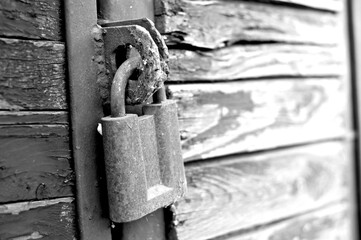 A black and white photograph of an old rusted lock sees on a wooden barn door. Prohibition concept. Protection against thieves and robbers, there is no way further. Fears hide under lock and key.