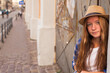 © De Visu - Long-haired girl standing on a street in shorts and hat.