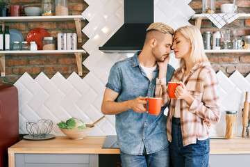 Young happy couple in love drink coffee in the morning embracing in kitchen at home. Relationship, family concept