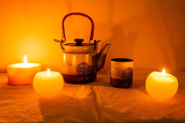 Sticker - Closeup shot of burning candles teapot and cups on dark background