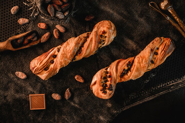 Wall Mural - Freshly backed twisted cakes or puff pastry buns with chocolate on rustic sackcloth background. Pastries and bakery, top view